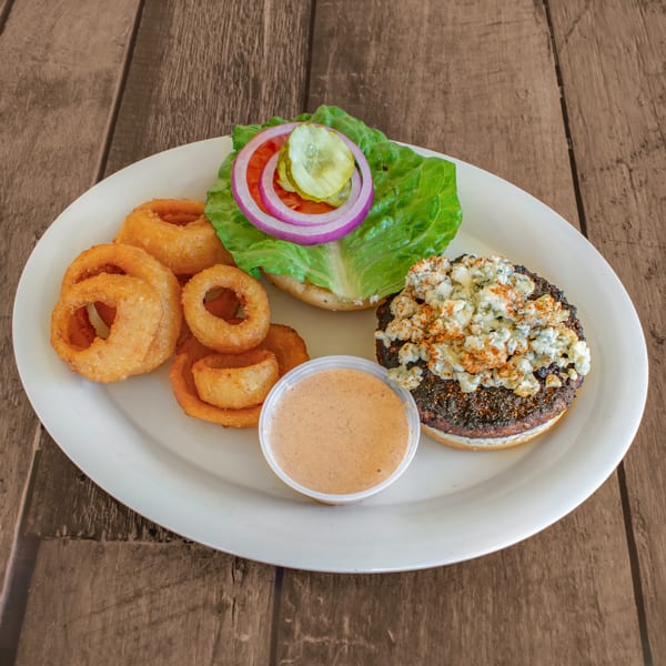 Open-faced burger with blue cheese, lettuce, tomato, onion, pickles, onion rings, and dipping sauce.
