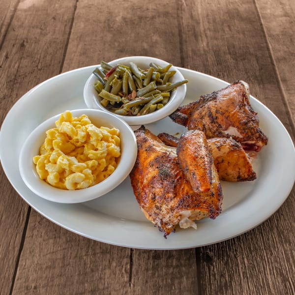 Grilled chicken pieces with sides of macaroni and cheese and green beans on a white plate.