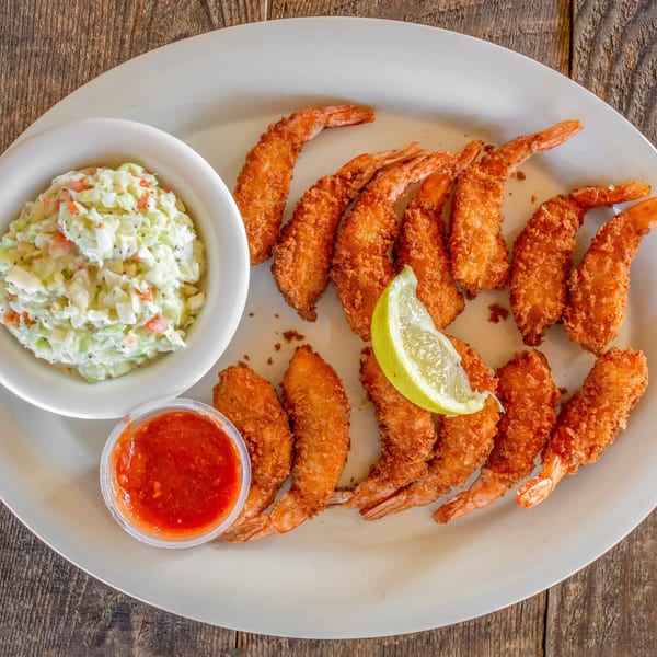 Crispy fried shrimp with coleslaw, cocktail sauce, and a lime wedge on a white plate.