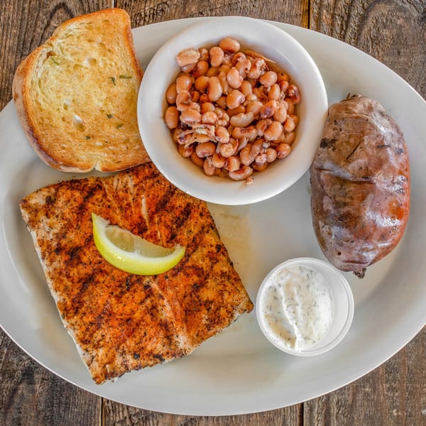 Grilled fish with a lemon wedge, garlic toast, a side of beans, and a baked sweet potato.