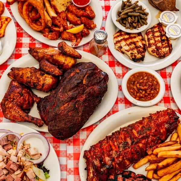 A red and white checkered table laden with various barbecue dishes, sides, and drinks.